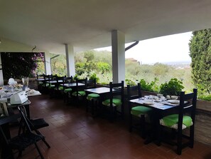 Un espacio de comedor al aire libre con mesas y sillas, rodeado de vegetación y con vistas panorámicas.