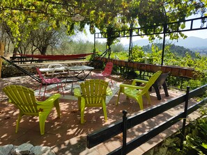 Un patio exterior con mesa y sillas, rodeado de follaje y una vista panorámica.