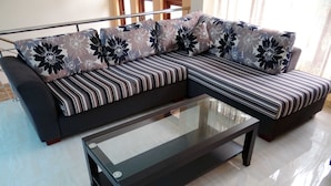 A modern living room with a sectional sofa, a glass coffee table, and a striped rug. - Dilray Villa (Harispattuwa)