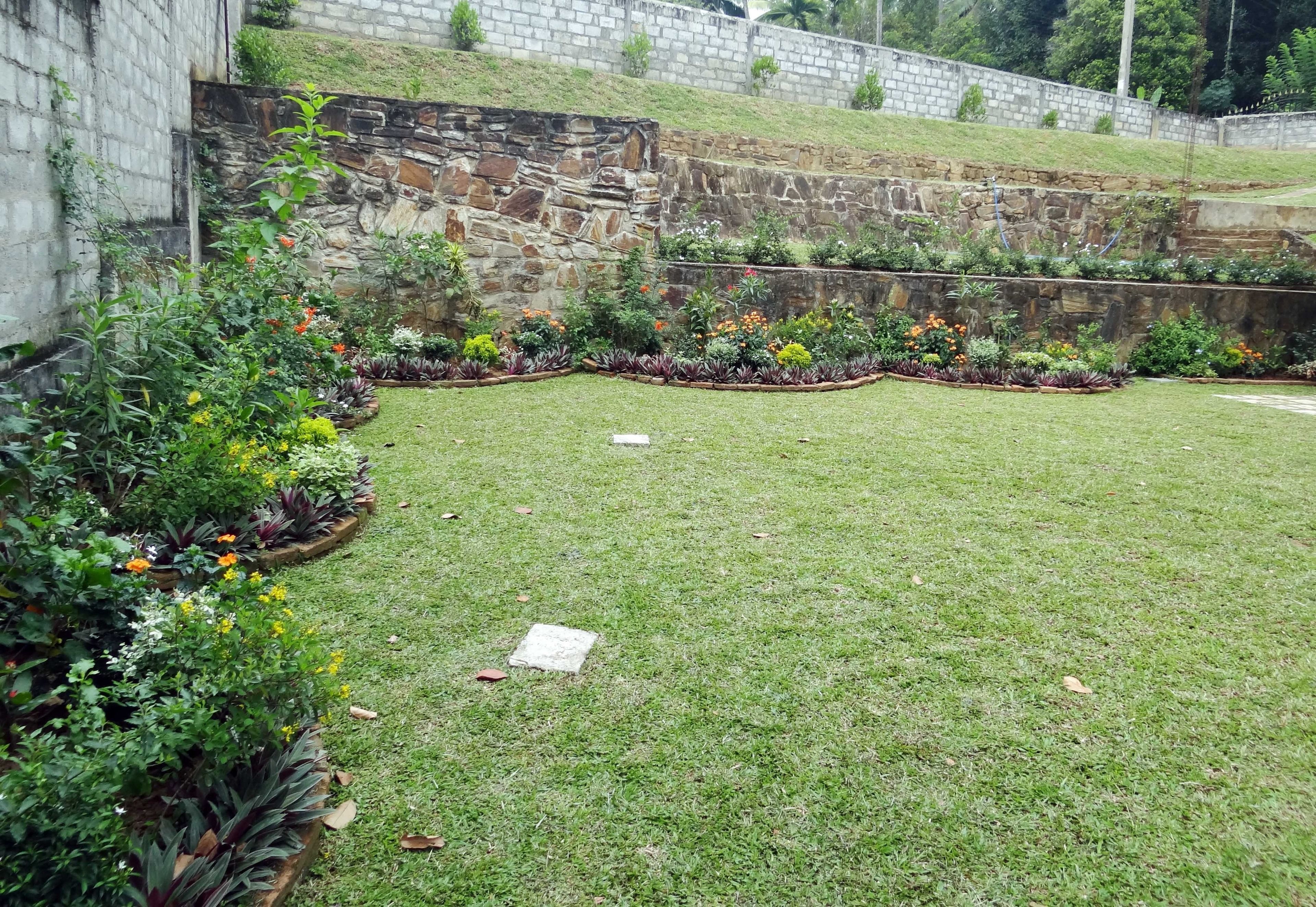Un jardin bien entretenu, agrémenté d’un mur en pierre, de diverses plantes à fleurs et d’une pelouse verdoyante.