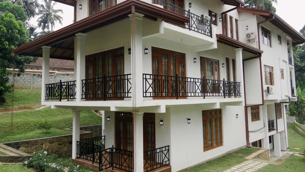 A multi-story residential building with balconies, a stone retaining wall, and a well-maintained lawn. - Dilray Villa (Harispattuwa)