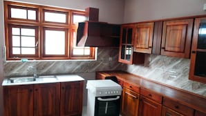 A kitchen with wooden cabinets, a built-in oven, and a window with multiple panes. - Dilray Villa (Harispattuwa)