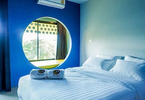 A hotel room with a large round window, a bed with white linens, and a pillow with a logo.