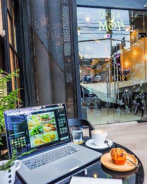 A laptop on a table with a muffin and a cup of coffee, a glass of water, and a potted plant. - Dejamoon (Chiang Mai)