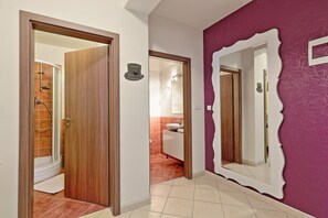 A hallway with a wooden door, a bathroom with a shower, and a mirror with a unique frame.