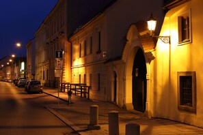A street at night with buildings, a bench, and a sign indicating a parking area.
