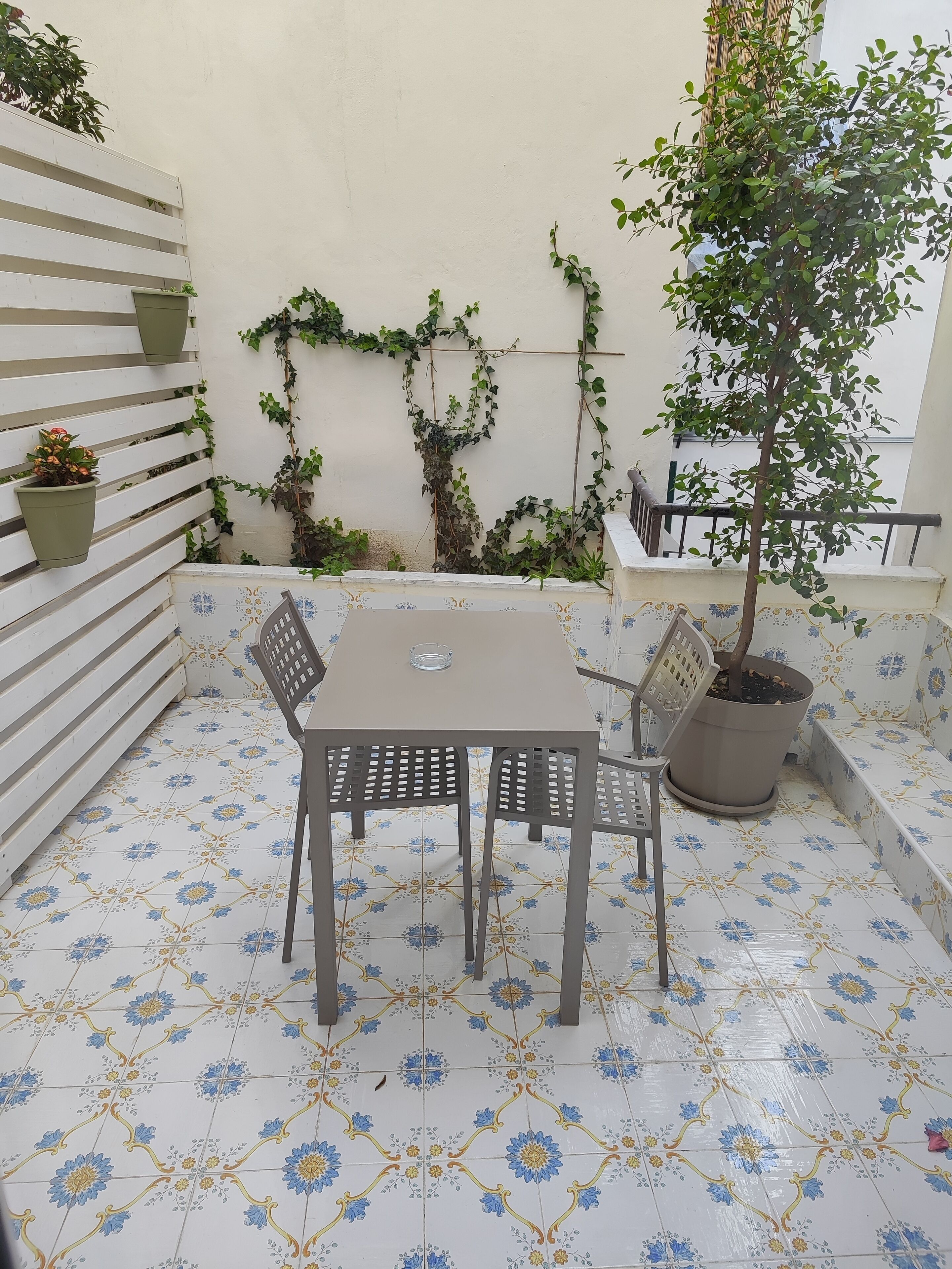 Eine Terrasse mit Tisch und Stühlen, Blumentöpfen und einem Fliesenboden.