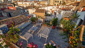 A rooftop terrace with potted plants, outdoor furniture, and a view of the surrounding buildings.
