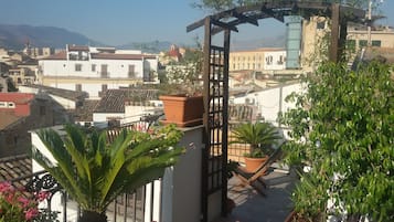 Eine Dachterrasse mit Topfpflanzen, einer Holzpergola und Blick auf die Stadtlandschaft.