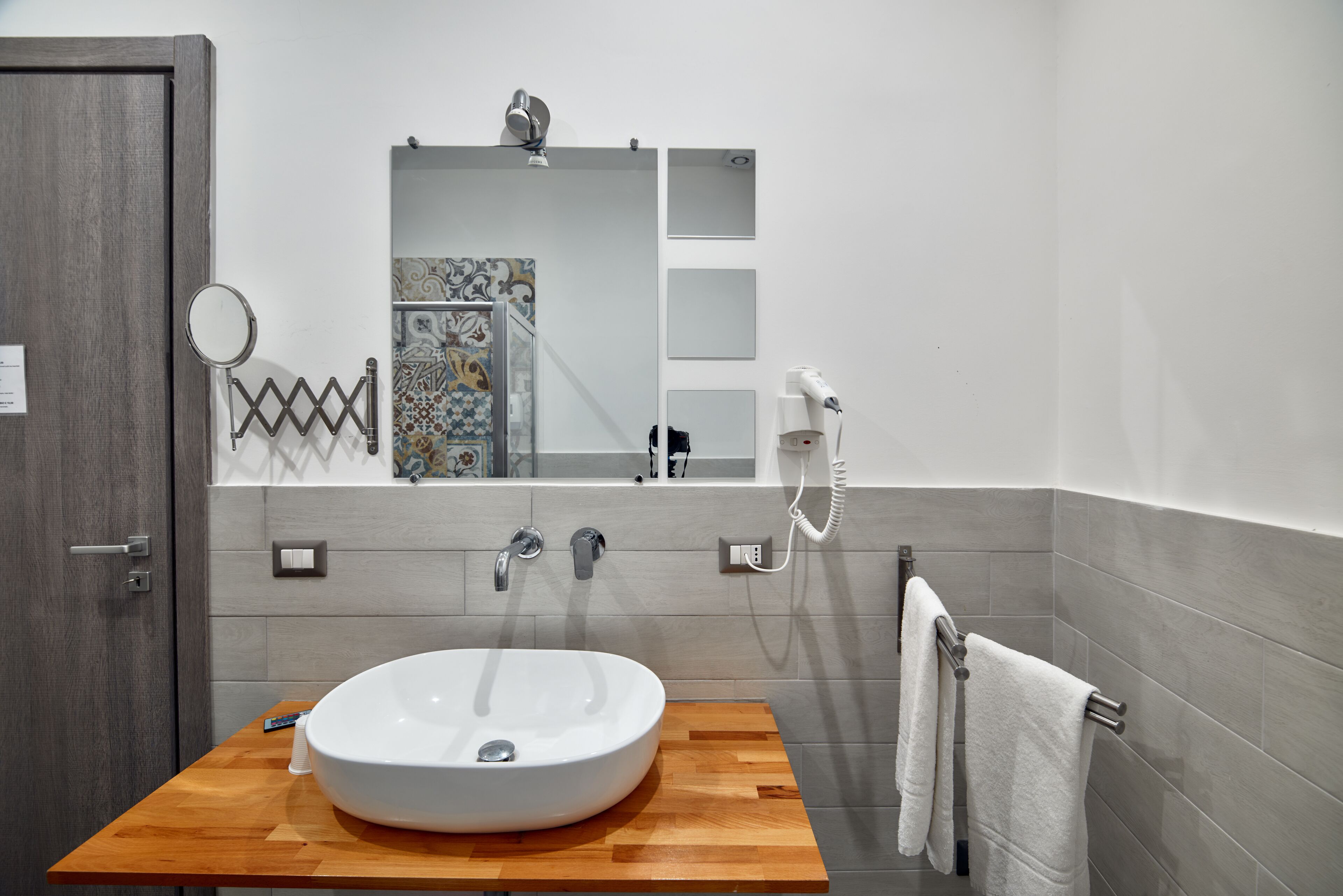 A bathroom with a wooden vanity, a white sink, a mirror, a towel rack, and a handheld mirror.