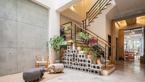 A spacious indoor area with a concrete wall, a staircase with plants, a wooden chair, and a concrete elephant sculpture. - Sun Moon Inn (Yuchi)