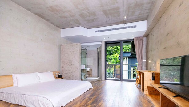 A modern bedroom with a large bed, wooden flooring, a TV, and a balcony with a view of greenery. - Sun Moon Inn (Yuchi)