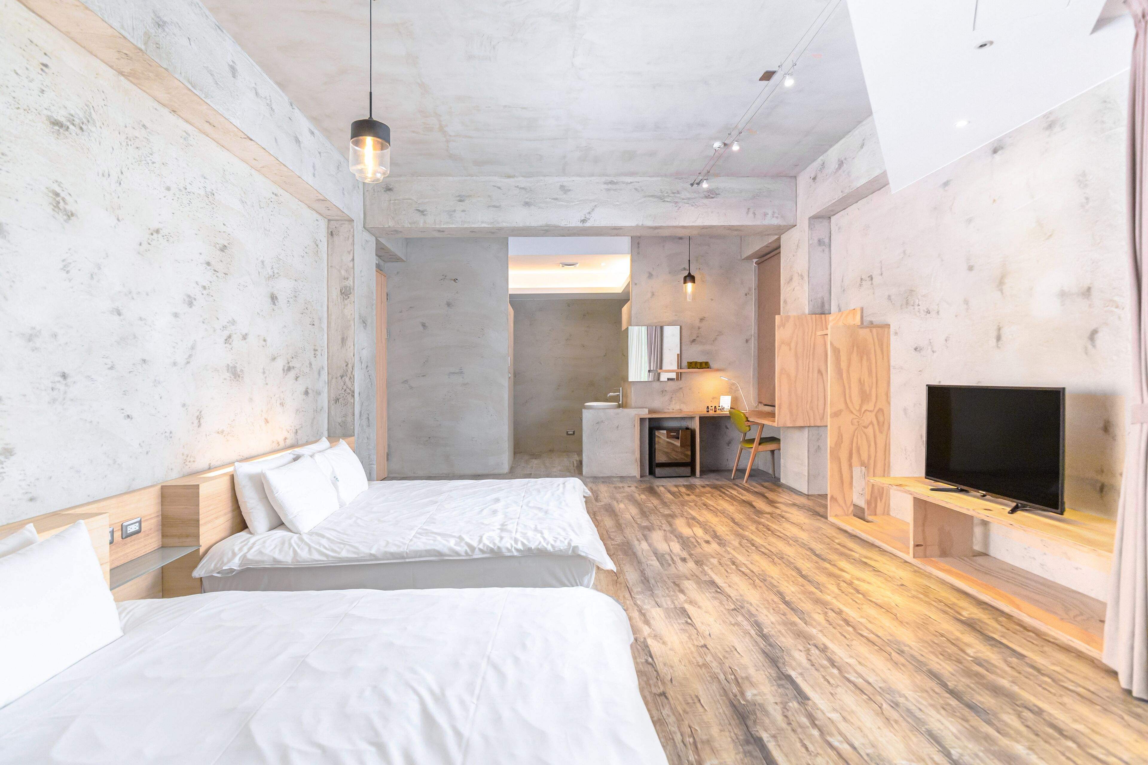 A modern hotel room with two beds, a wooden floor, a TV, and a small desk area.