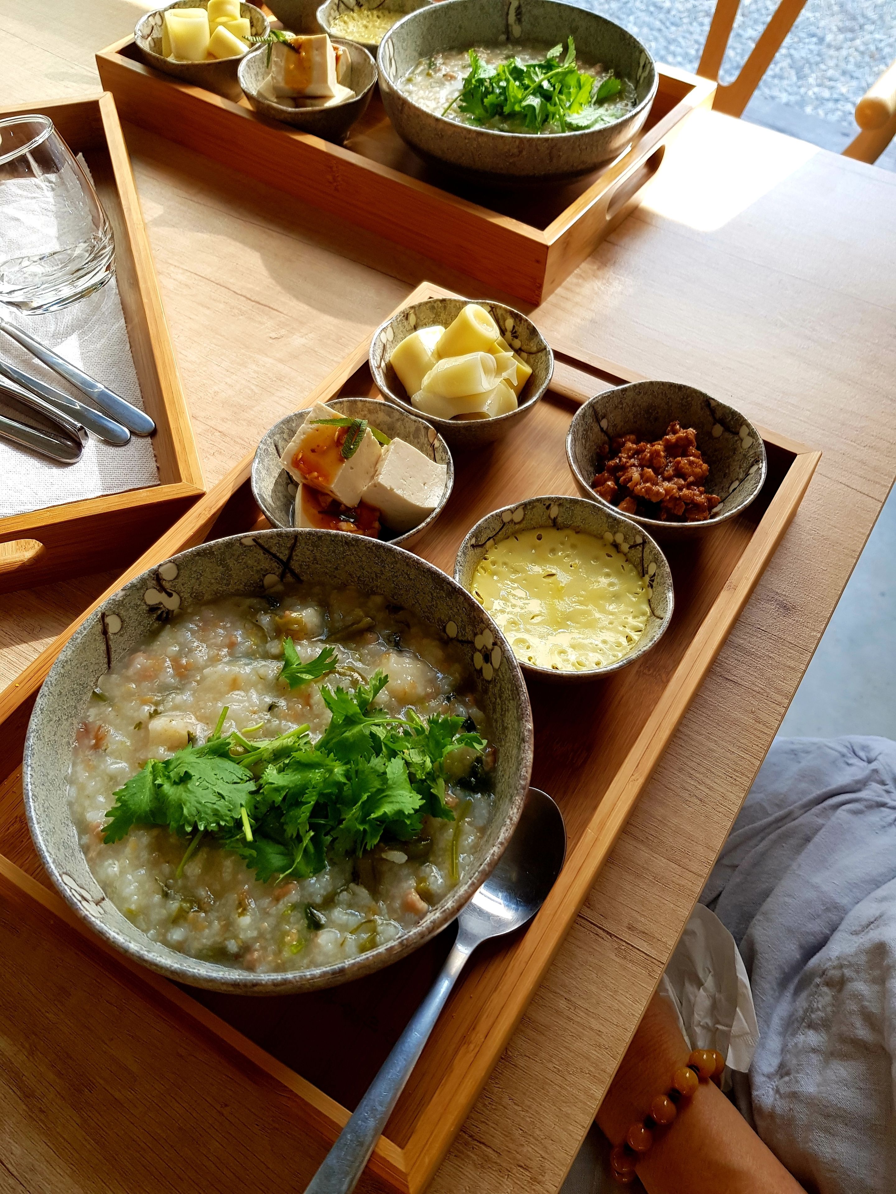 A wooden table with various bowls of food, including a bowl of soup garnished with cilantro, a bowl of tofu, and several small dishes with different ingredients.