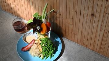 Un plato con fideos, verduras verdes, una salchicha y un vaso de líquido oscuro.
