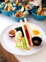 Un plato con un huevo frito, una rodaja de tomate, una rebanada de pan, un recipiente pequeño con salsa y media fruta cortada.