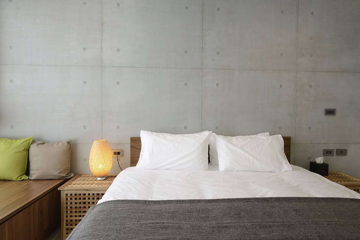 A neatly made bed with white linens, a bedside lamp, and a wooden nightstand with a tissue box.