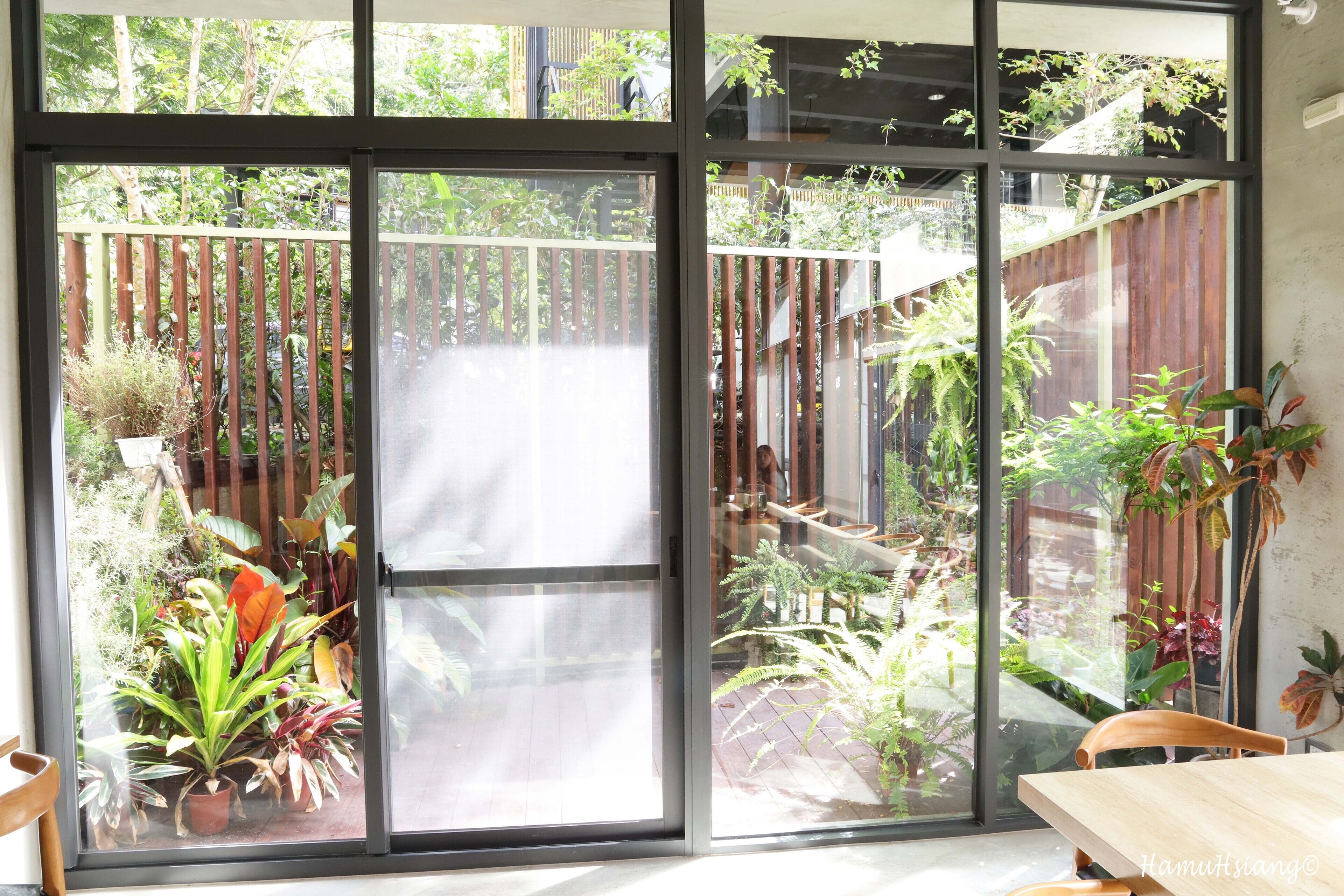 A room with large sliding glass doors leading to a garden with various plants and a wooden deck.