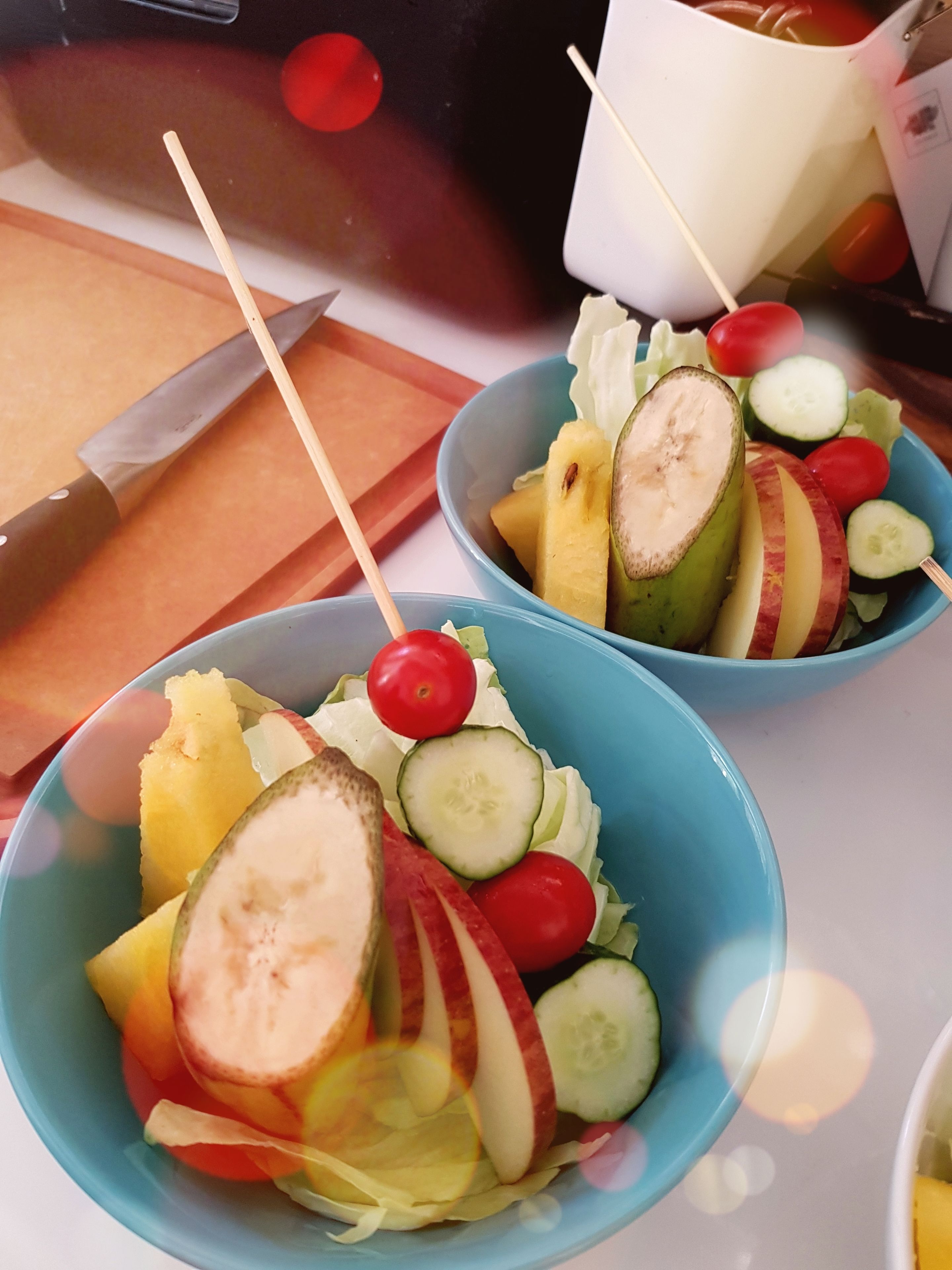 Two bowls of fruit salad with a knife and a cutting board in the background.