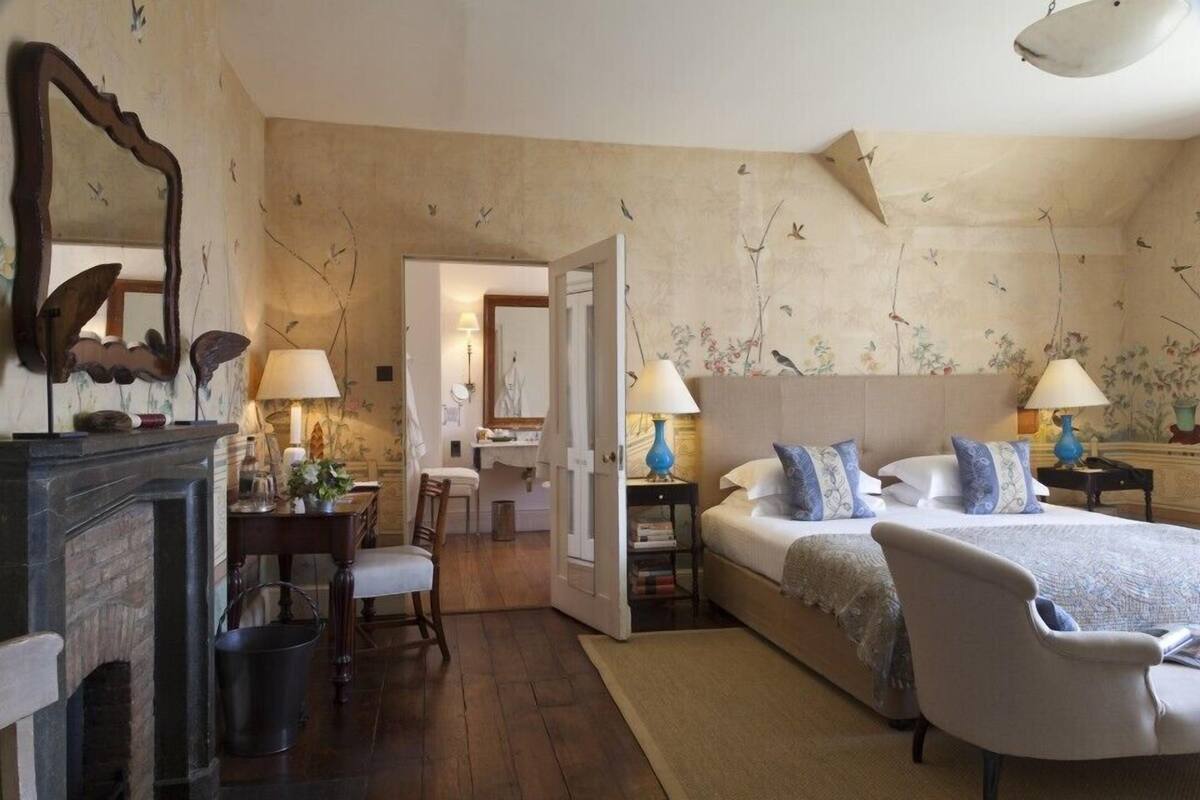 Un dormitorio con dos camas, una chimenea, un espejo y una puerta que da a un baño.