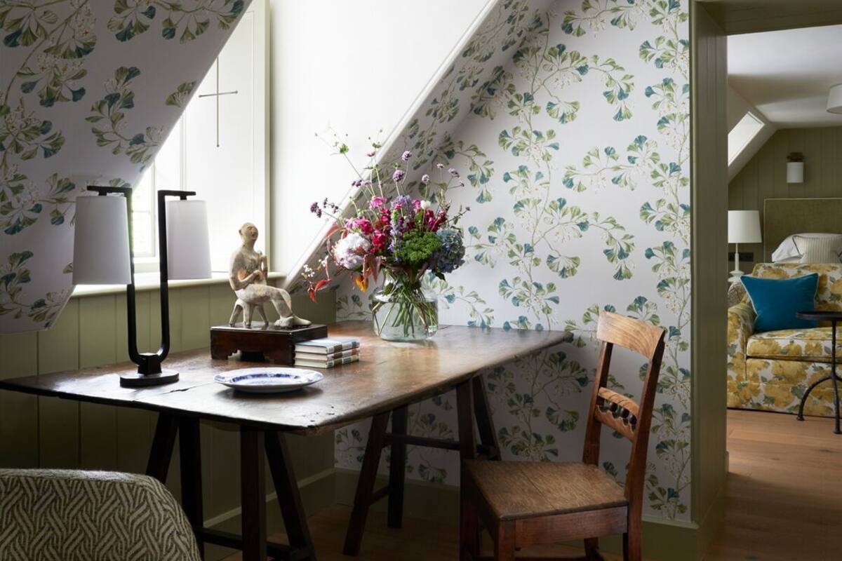 Un comedor con una mesa de madera, sillas, un jarrón de flores y una lámpara.