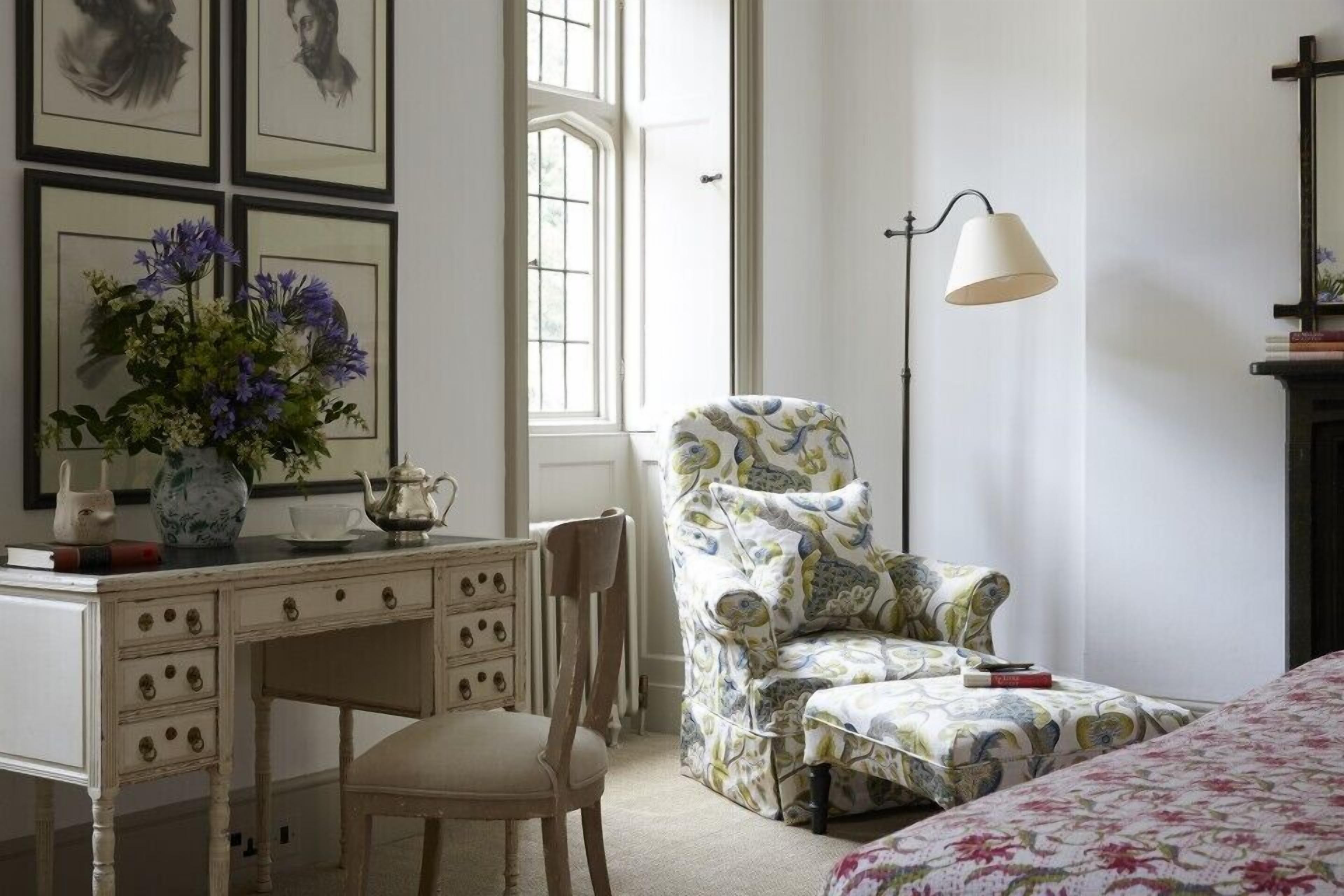A bedroom with a bed, a desk with a vase of flowers, a chair, and a lamp.
