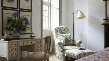 A bedroom with a bed, a desk with a vase of flowers, a chair, and a lamp.