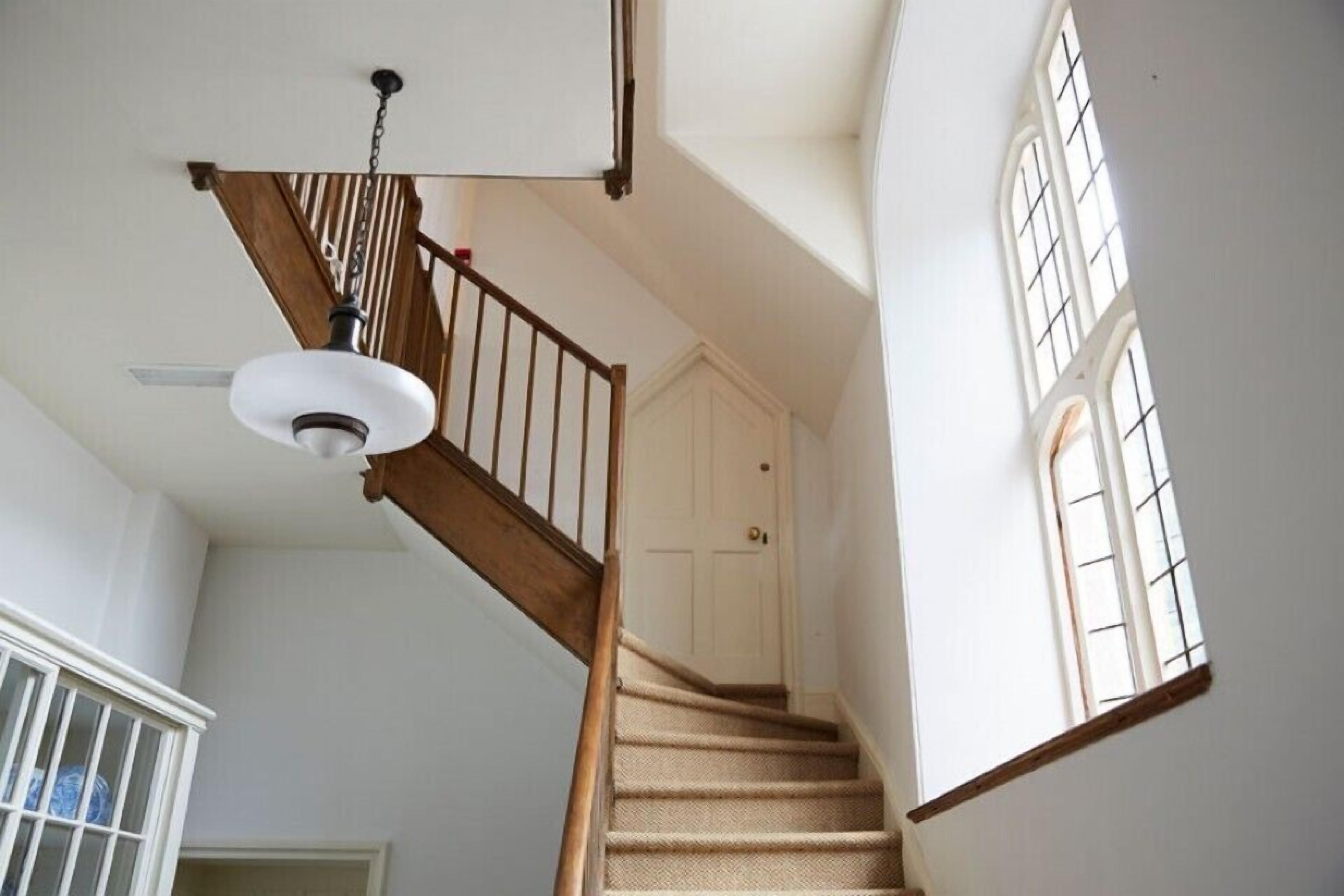 Una escalera con barandilla de madera y alfombra color crema, que conduce a una puerta blanca.
