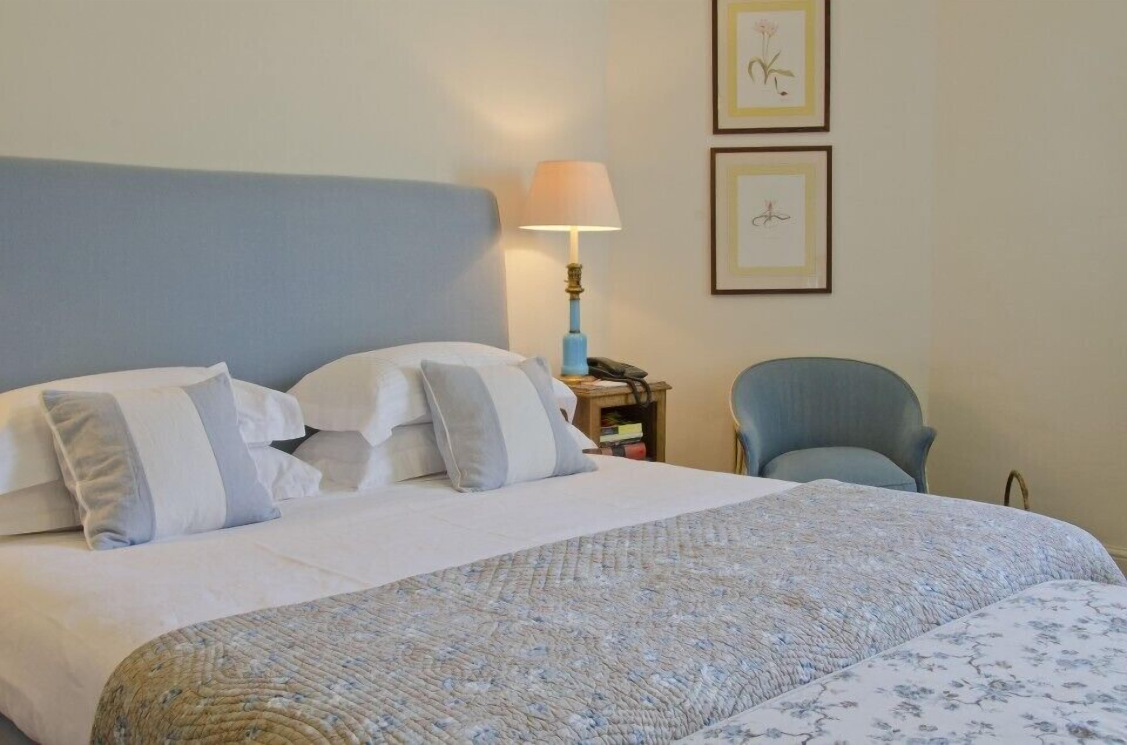A neatly made bed with a blue headboard, a bedside lamp, and a chair.