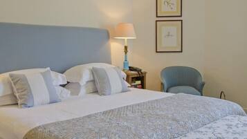 A neatly made bed with a blue headboard, a bedside lamp, and a chair.