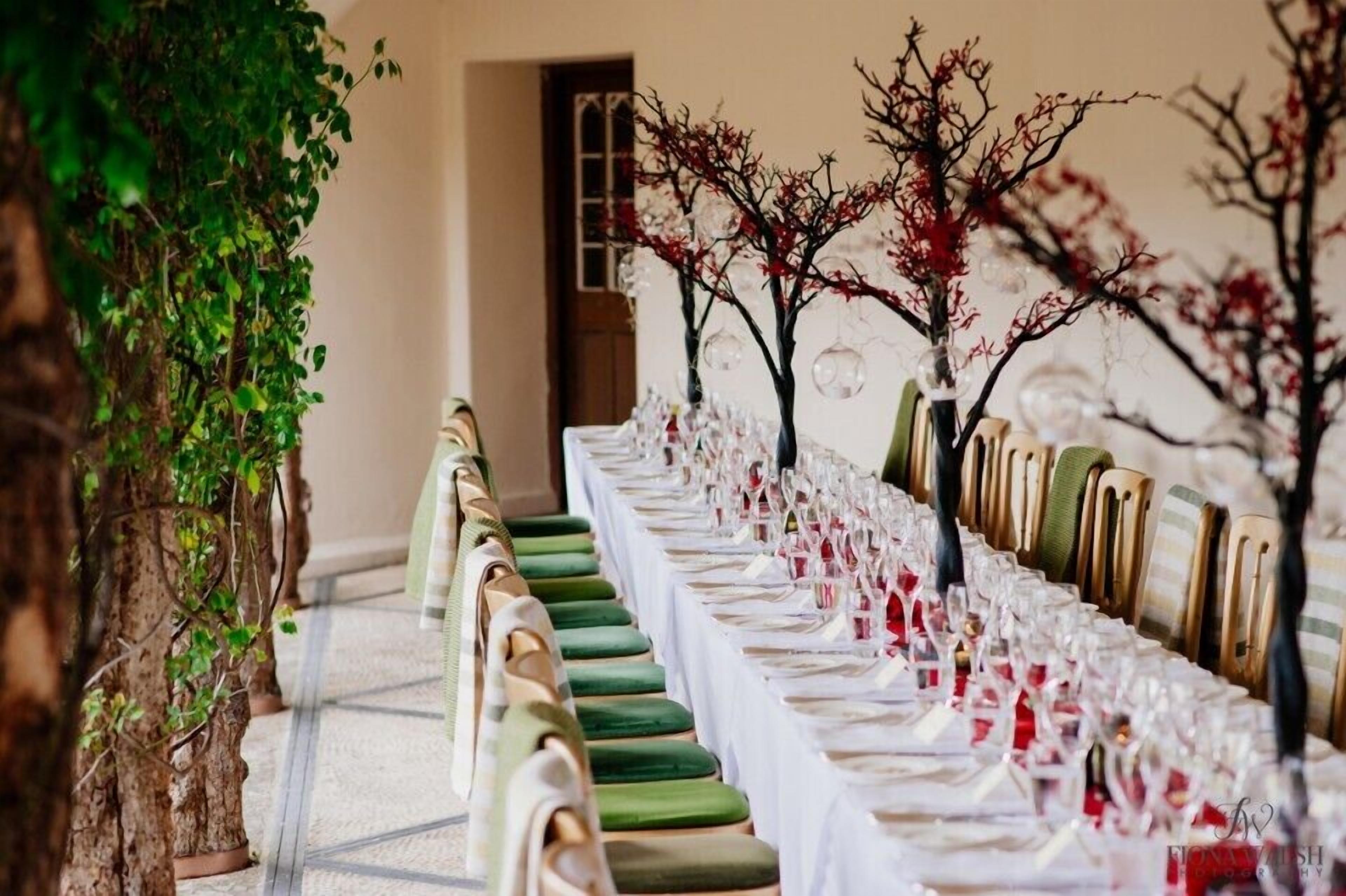 A long dining table set with chairs, glassware, and red napkins.