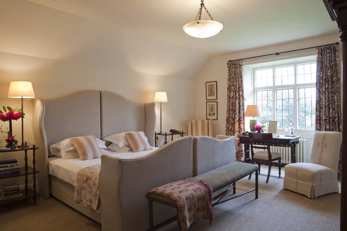Un dormitorio con cama, mesitas de noche, escritorio, silla y ventana con cortinas.