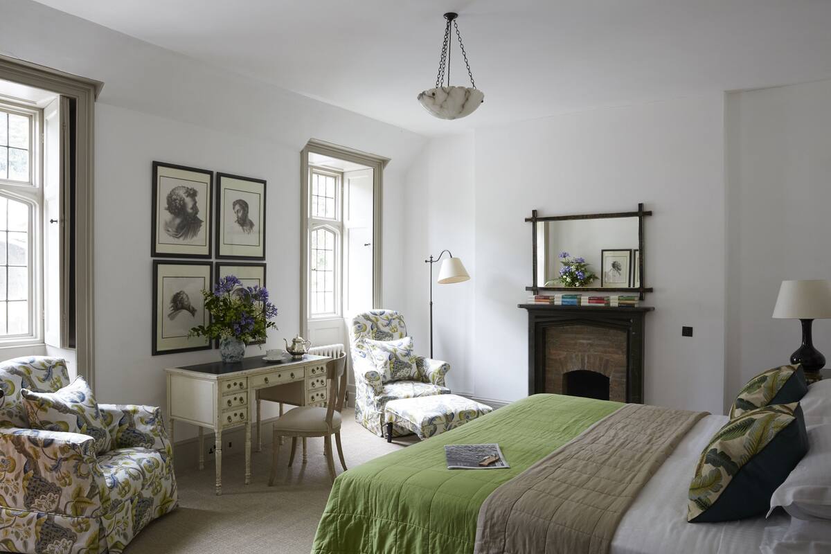 Un dormitorio bien iluminado con una cama, un escritorio, una silla y una chimenea.