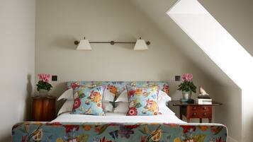 A bedroom with a bed, floral bedding, a nightstand with a plant, and a wall-mounted lamp.