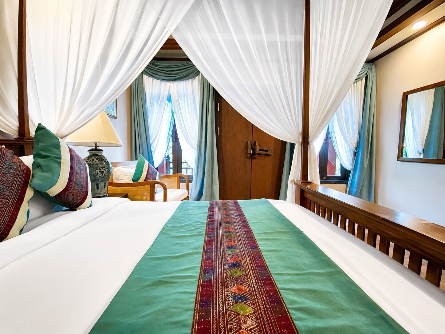 Uma cama com colcha verde, cortinas brancas e cabeceira de madeira.