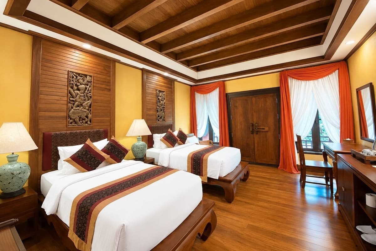Une chambre d’hôtel avec deux lits, des têtes de lit en bois, un bureau et une armoire.