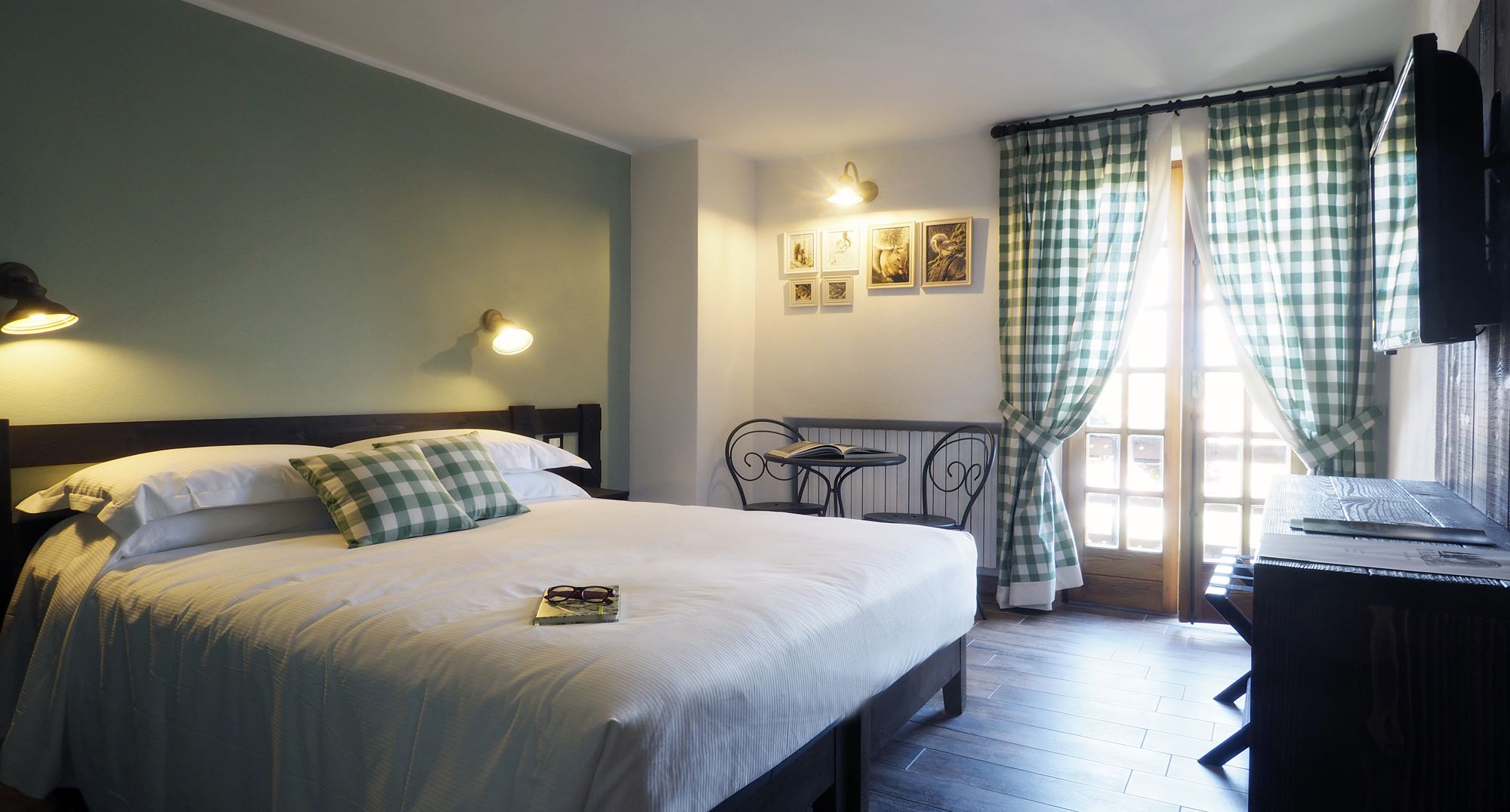 A neatly made bed with checkered pillows, a bedside table with a book, and a wall-mounted light fixture.