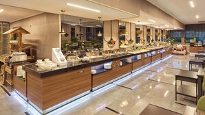 Un moderno vestíbulo de hotel con una larga mesa de buffet, área de descanso y un chef preparando comida.