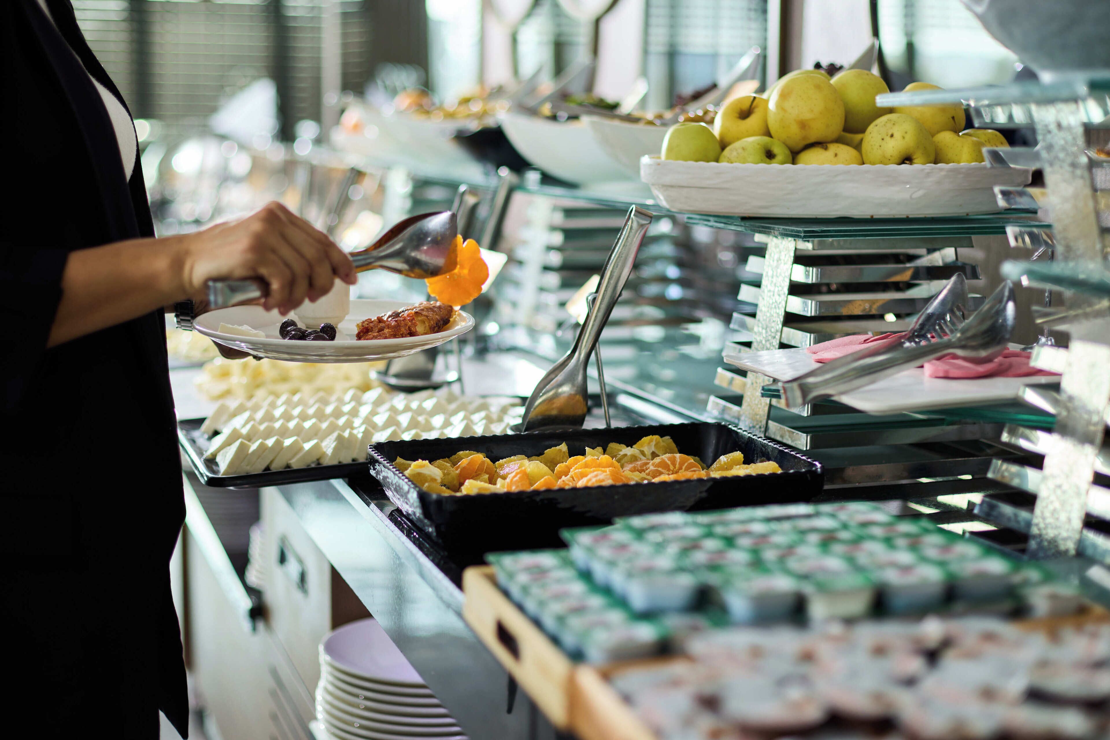 Un bufé con diferentes opciones de comida y una persona servándose.