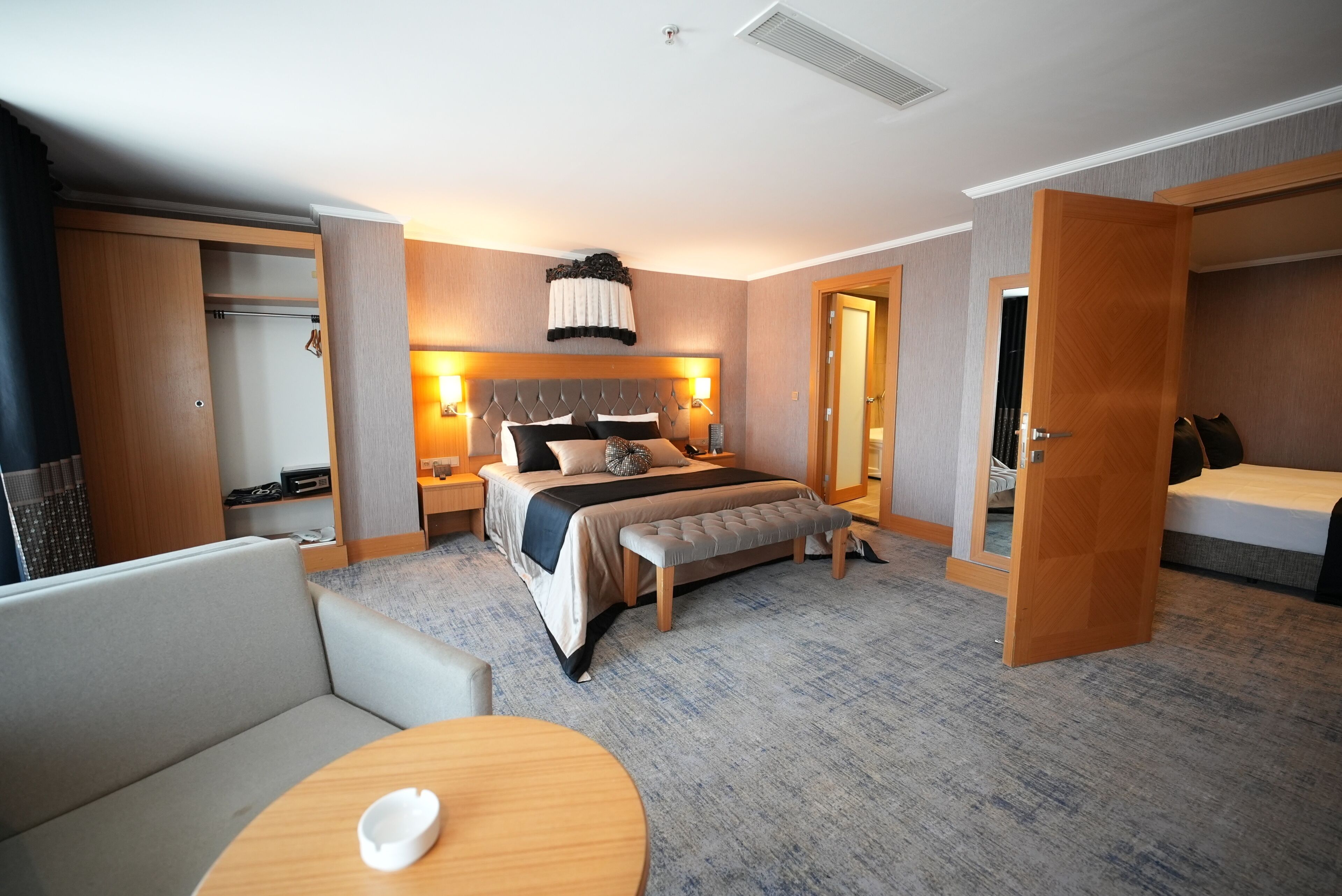 Ein Hotelzimmer mit Bett, Nachttischen, einer Sitzecke, einem Kleiderschrank und einer Tür zu einem weiteren Raum.