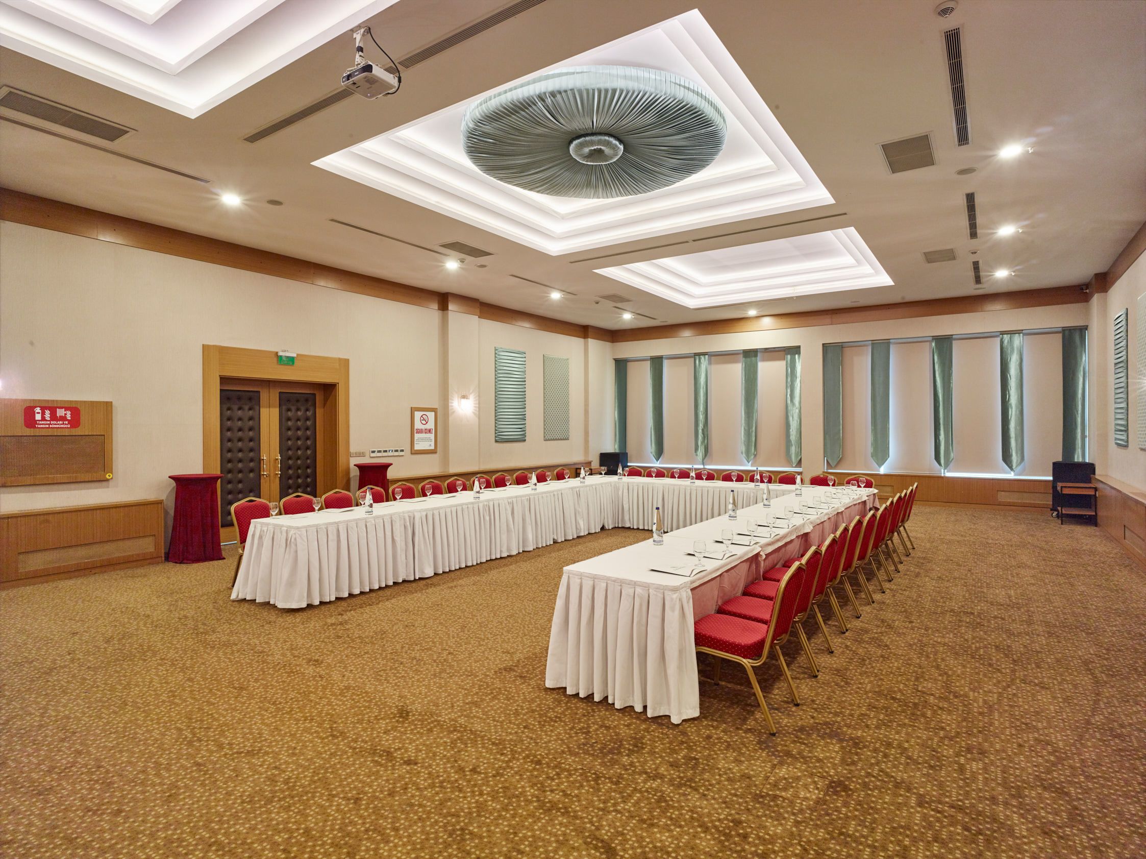 Uma sala de conferências com uma mesa comprida, cadeiras vermelhas e um ventilador de teto.