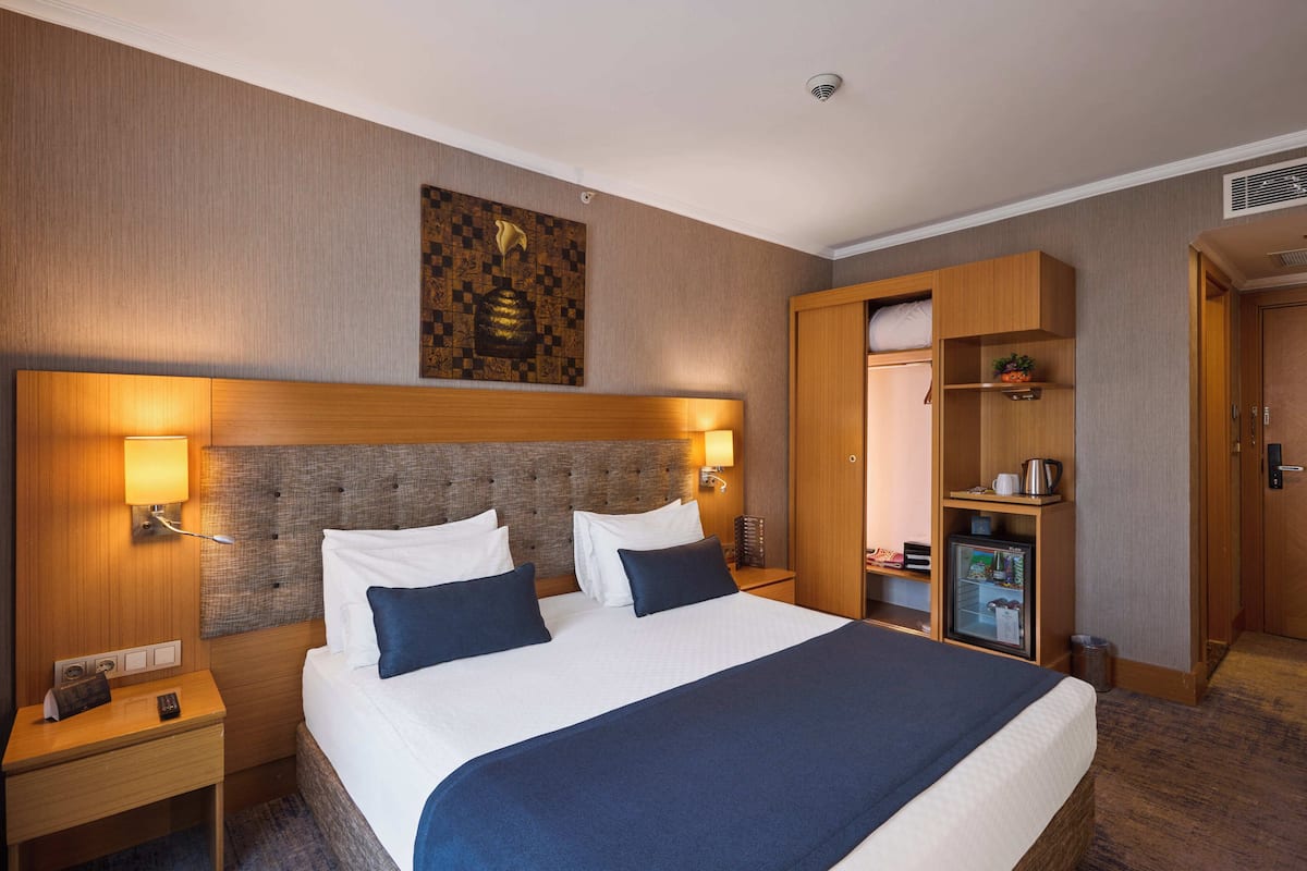 Una habitación de hotel con una cama grande, dos mesitas de noche, un armario y un minibar.