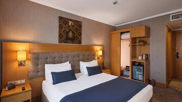 A hotel room with a large bed, two bedside tables, a wardrobe, and a minibar.