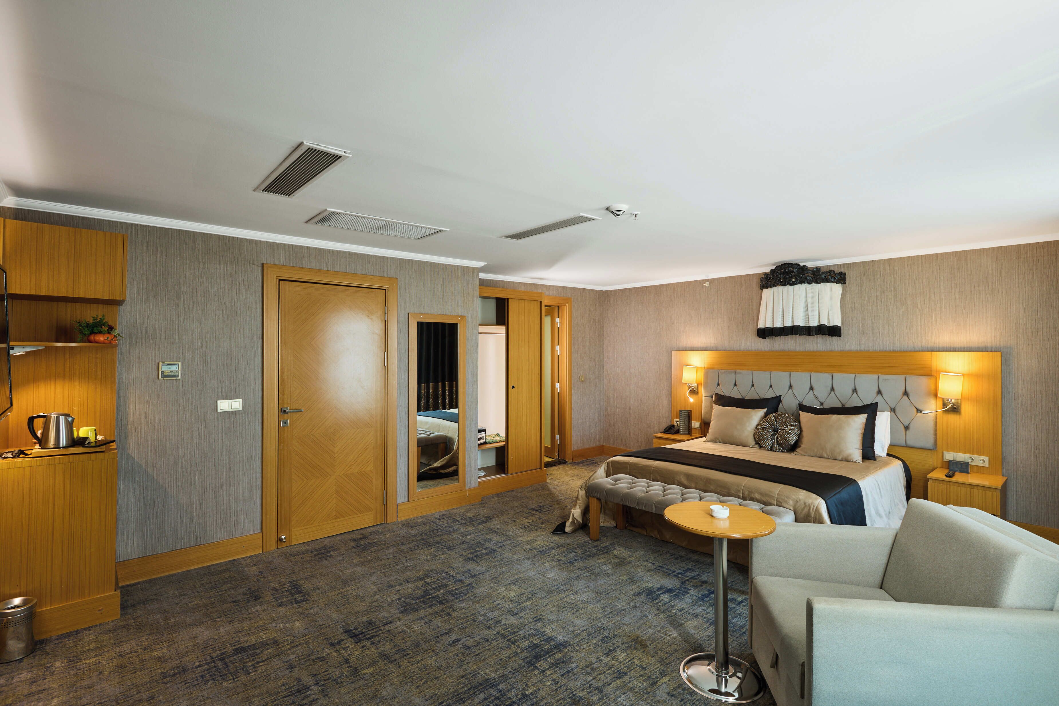 Een hotelkamer met een bed, nachtkastje, lamp en een klein rond tafeltje.