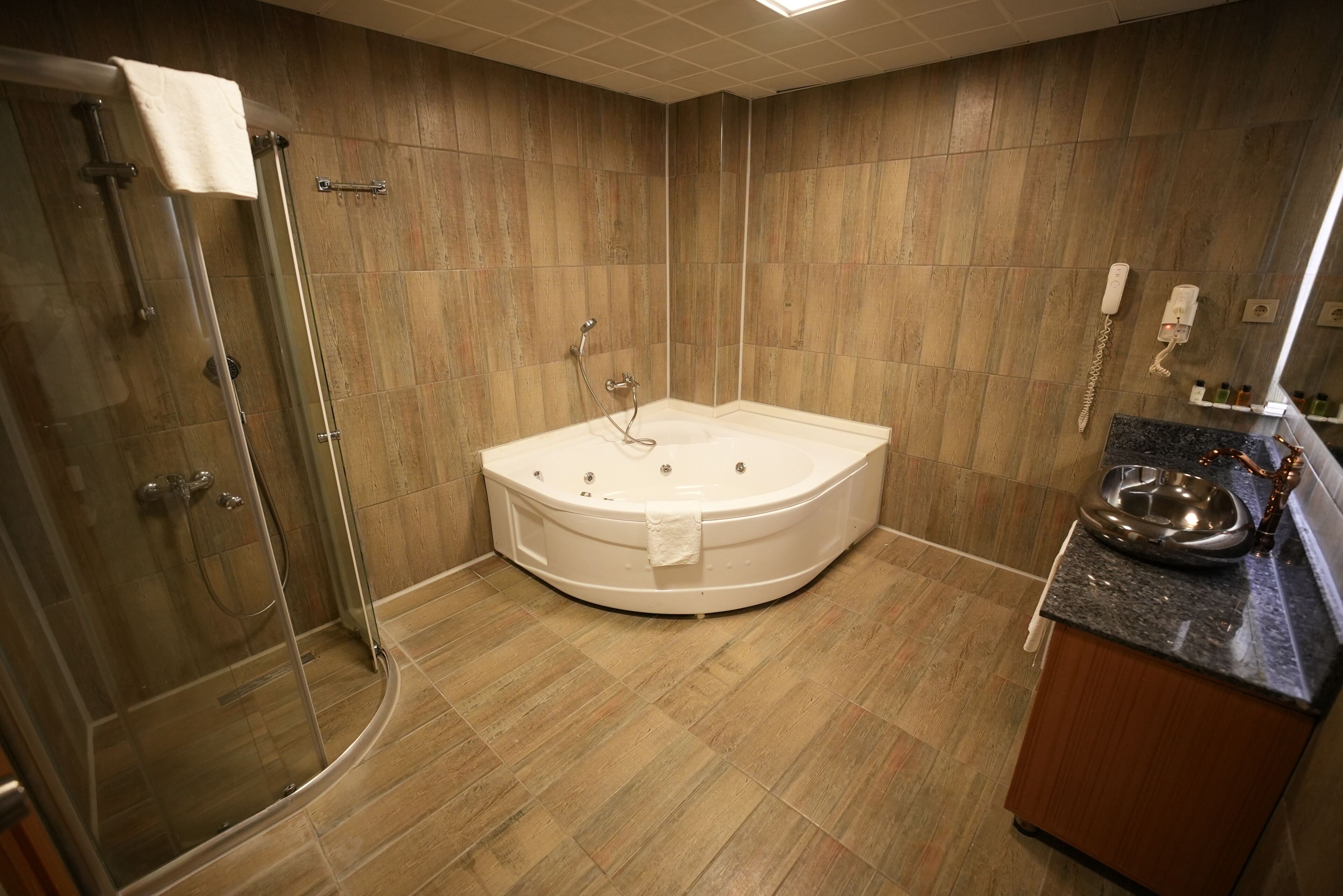 Un baño moderno con ducha envuelta en vidrio, una bañera independiente y encimera de granito con lavamanos y lavabo metálico.