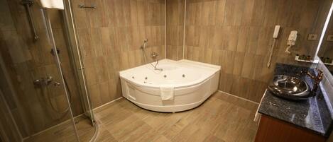 Un baño moderno con ducha envuelta en vidrio, una bañera independiente y encimera de granito con lavamanos y lavabo metálico.