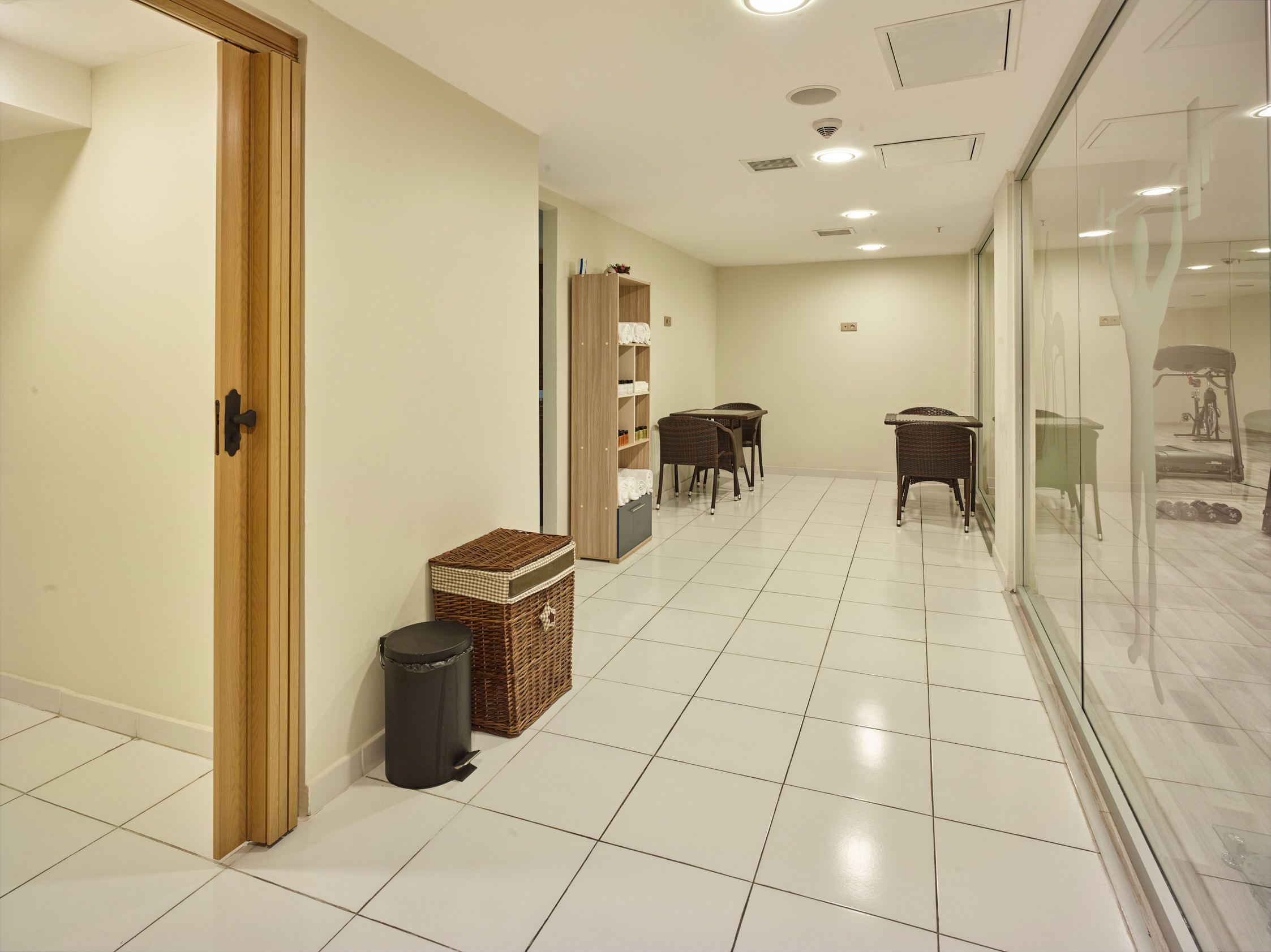 A hallway with a wooden door, a trash bin, a wicker basket, a bookshelf, and a table with chairs.