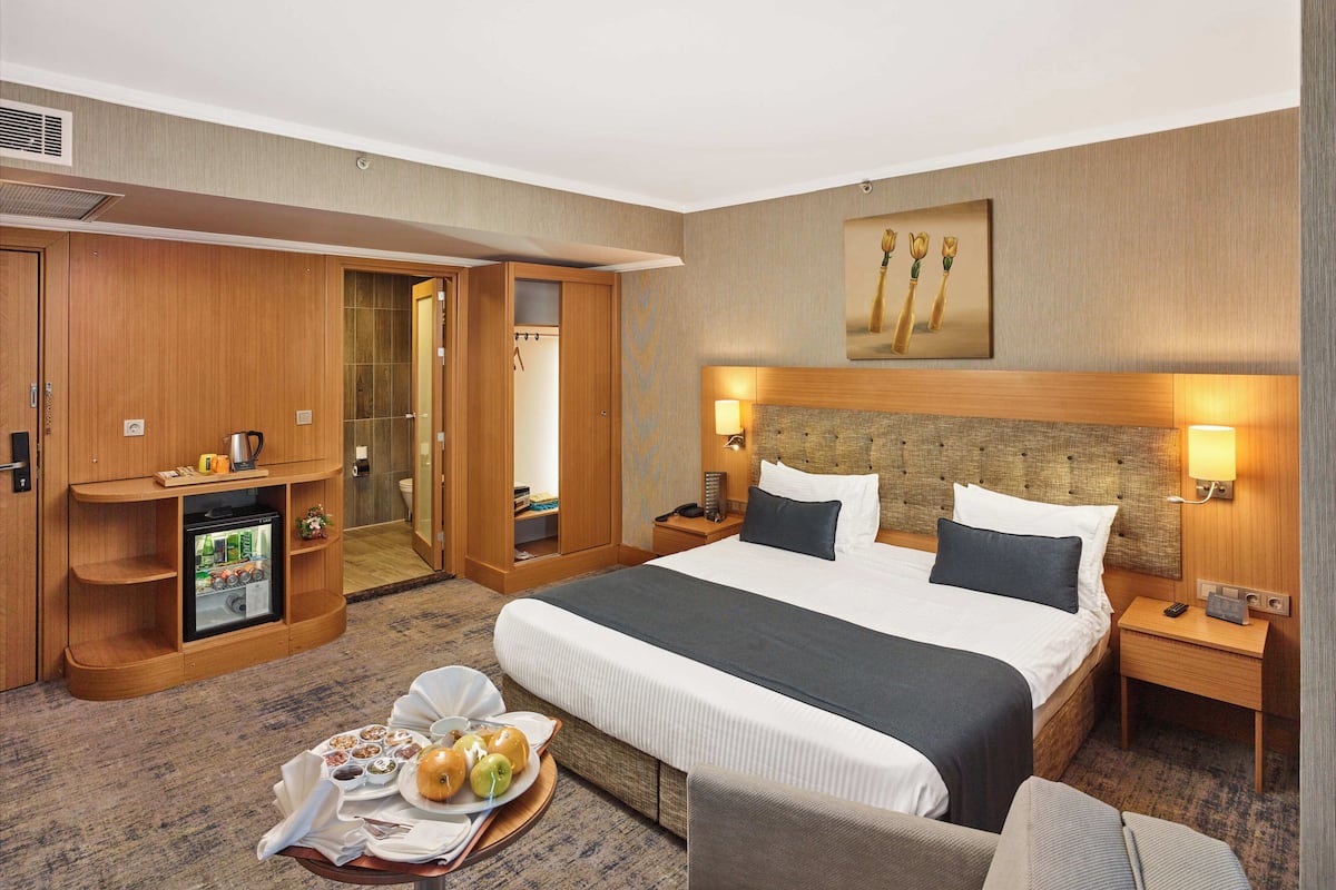 Habitación de hotel con una cama grande, un escritorio con computadora, un refrigerador pequeño y una bandeja para el desayuno.