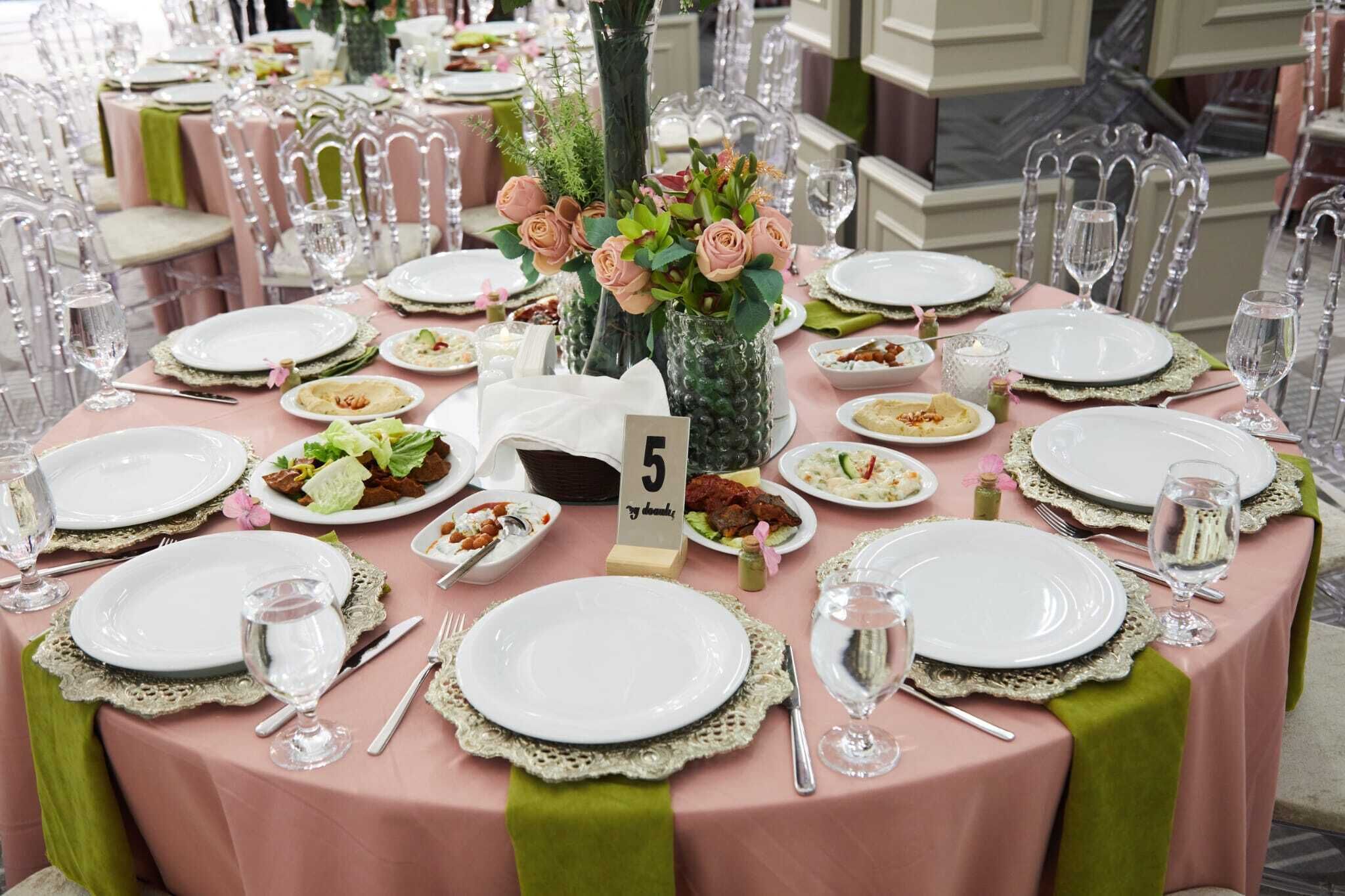 A round dining table with white plates, green tablecloths, and clear glassware.