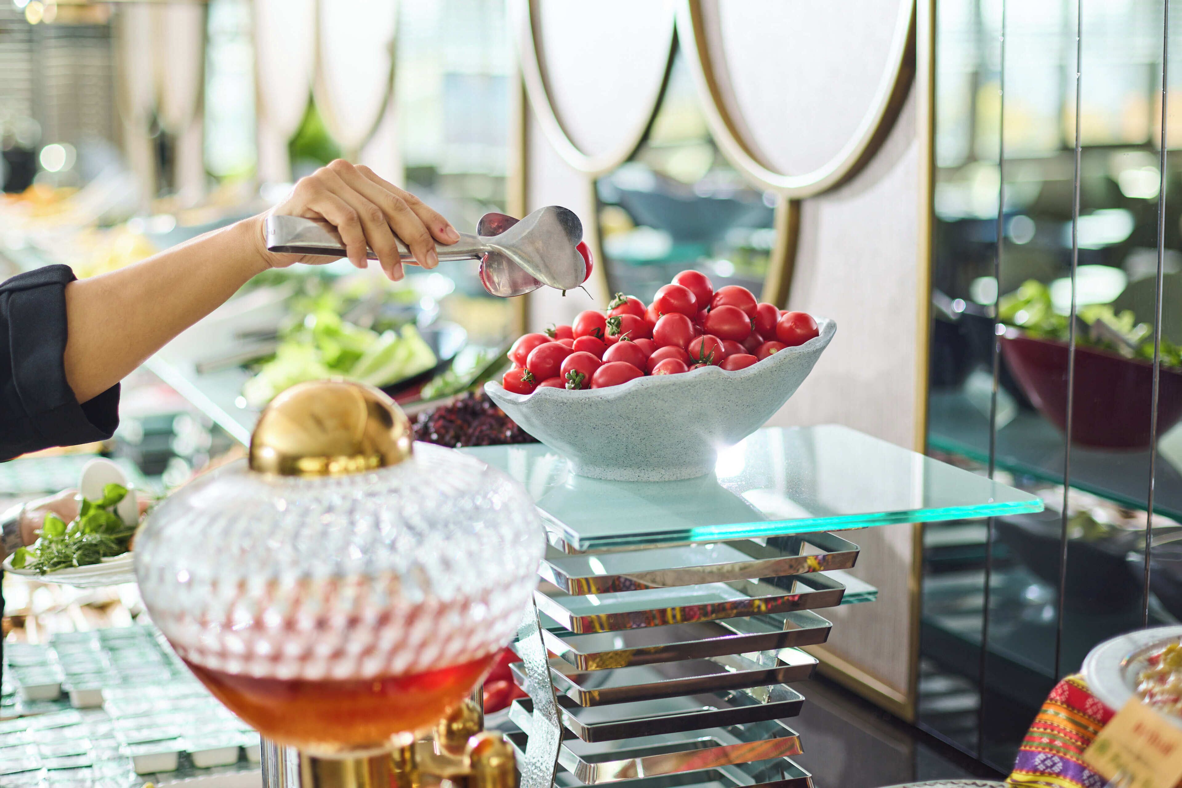 A buffet setup with a variety of food items, including a bowl of red tomatoes and a decorative glass bowl.